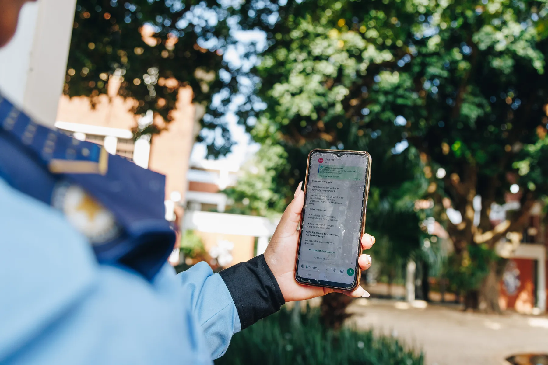 A Marshall Security officer in a blue uniform holds a phone displaying the Jem WhatsApp conversation