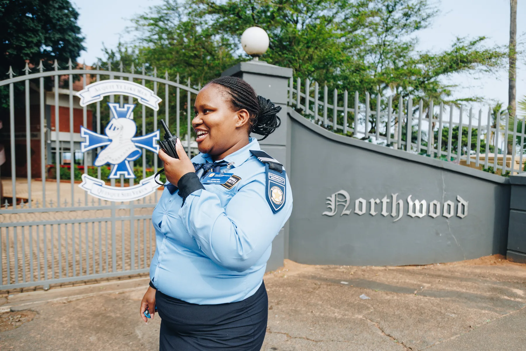 Anathi in her blue Marshall Security uniform speaks into a radio at the Northwood High School entrance