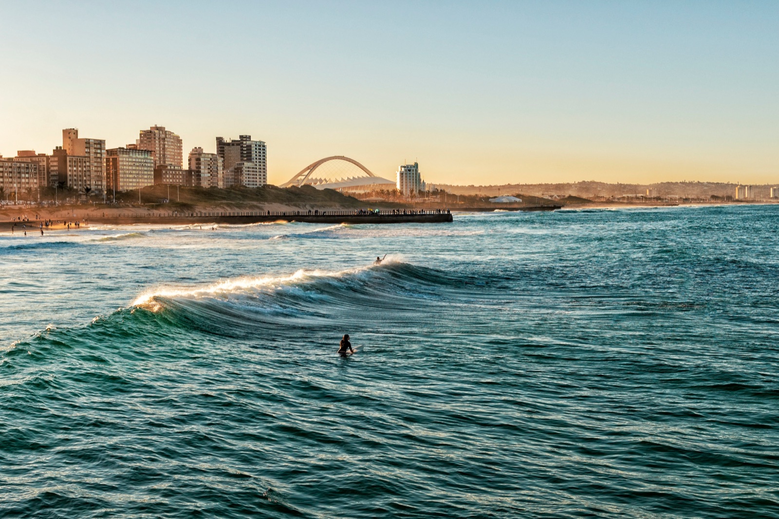 A surfer paddling out at Durban beachfront, with the Moses Mabhida arch on the skyline