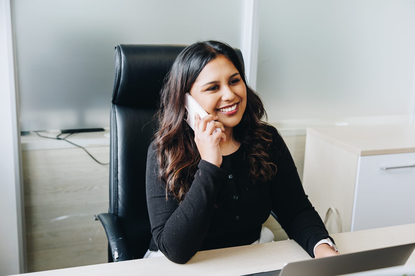 A Jem colleague smiling on a phone call at her desk, a laptop open in front of her