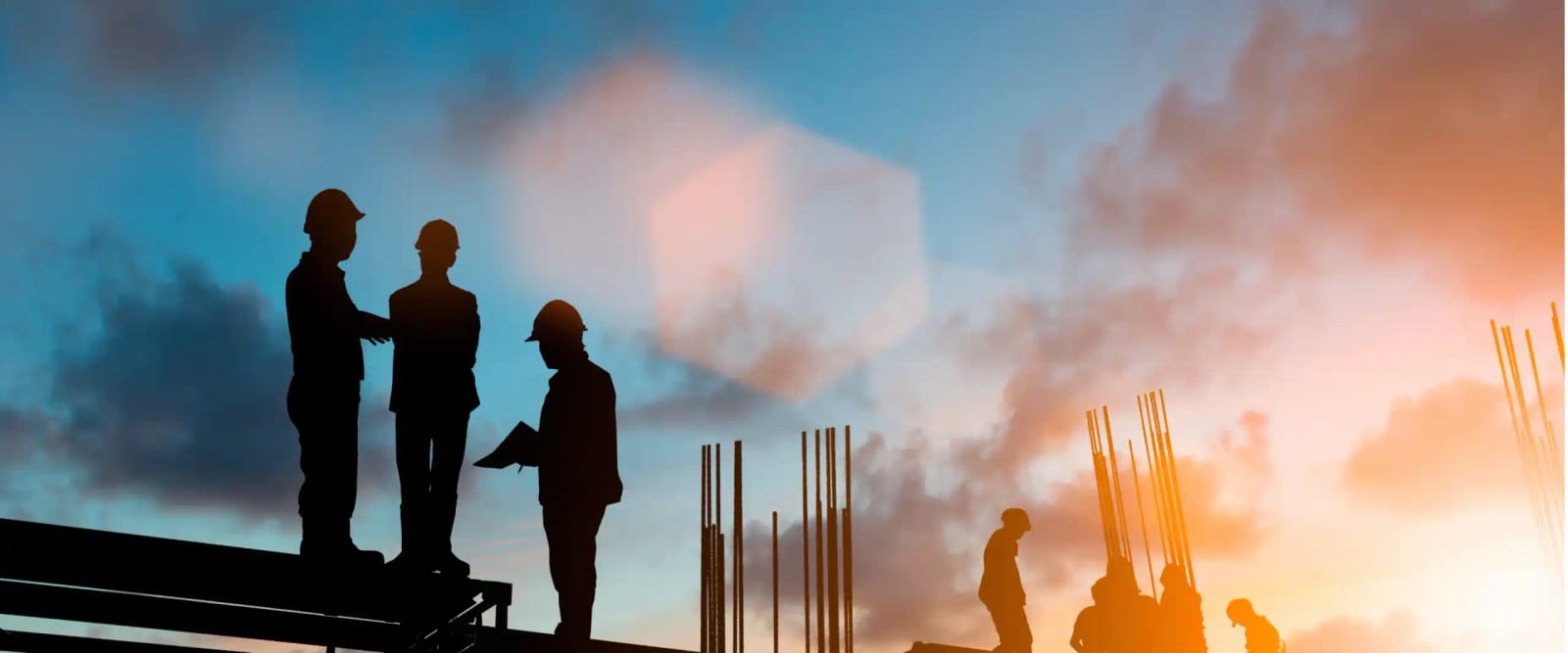 Construction workers silhouetted on a steel frame against a sunset