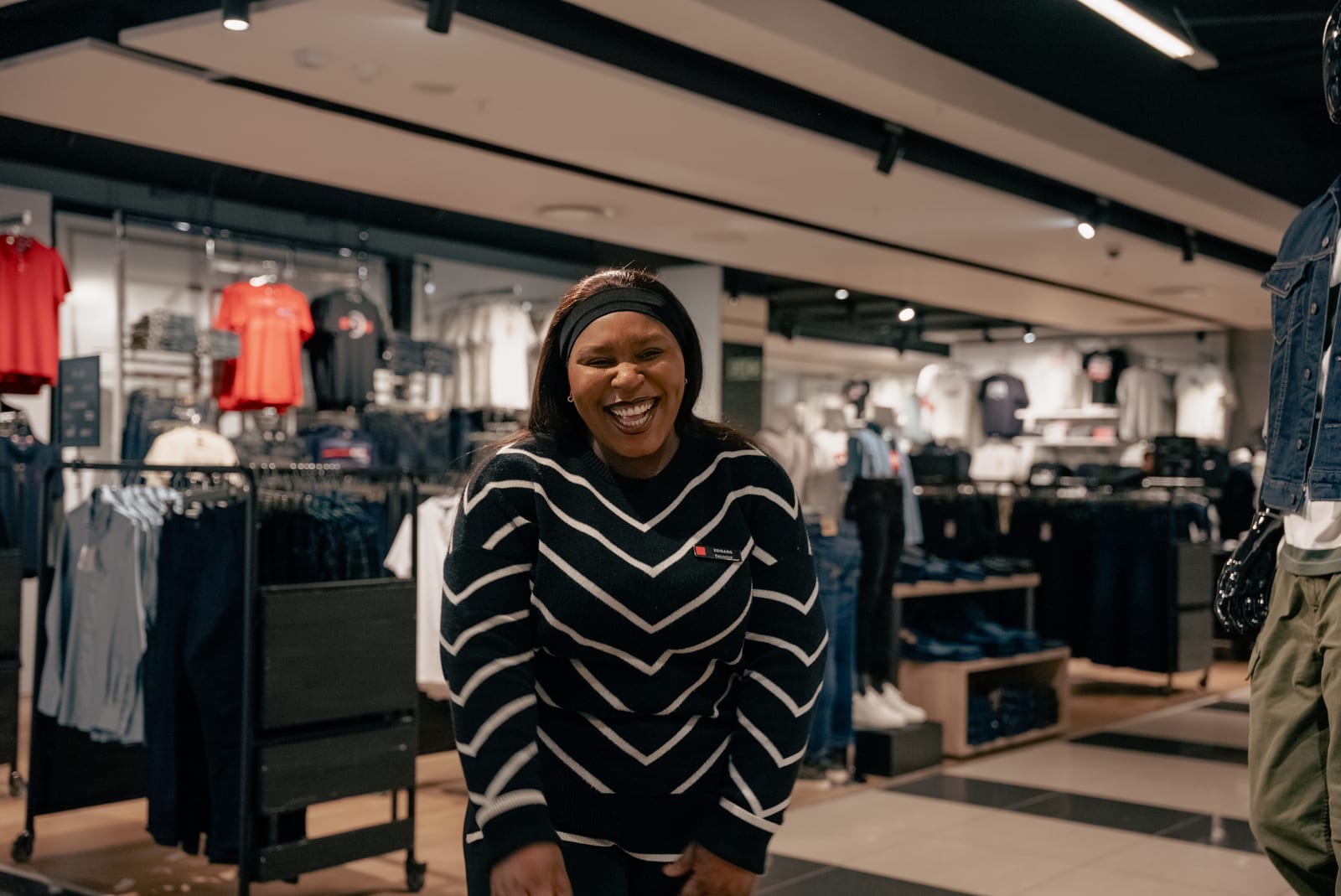 An Edgars retail assistant laughing on the shop floor between clothing rails