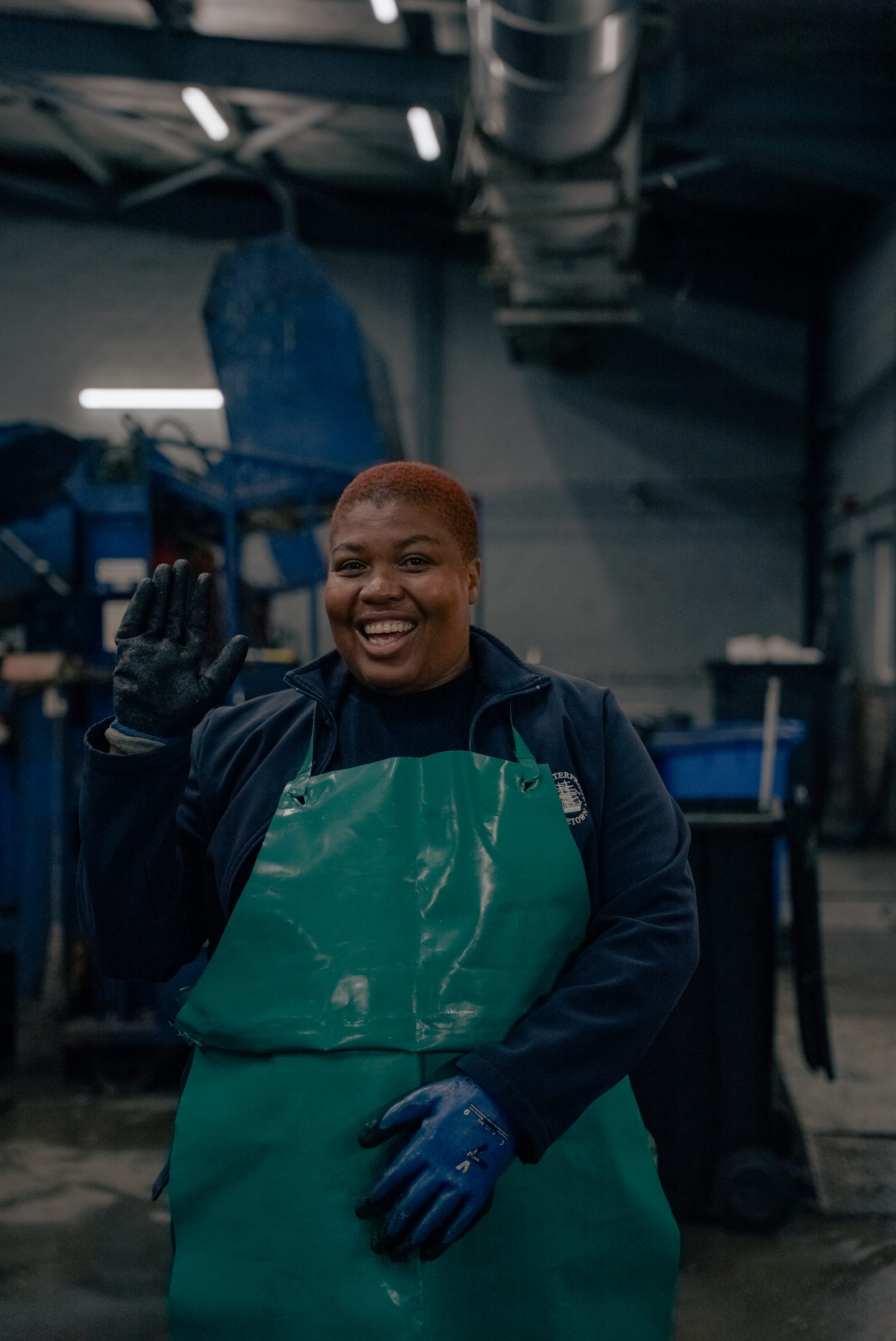 A waste sorting worker in an apron and gloves waving inside a recovery facility